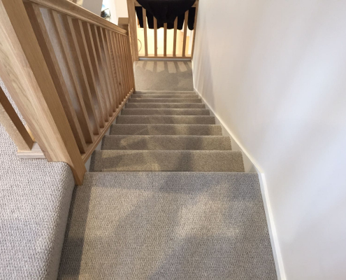 Wool loop Berber carpet fitted on staircase with quarter landing, white walls and oak bannister