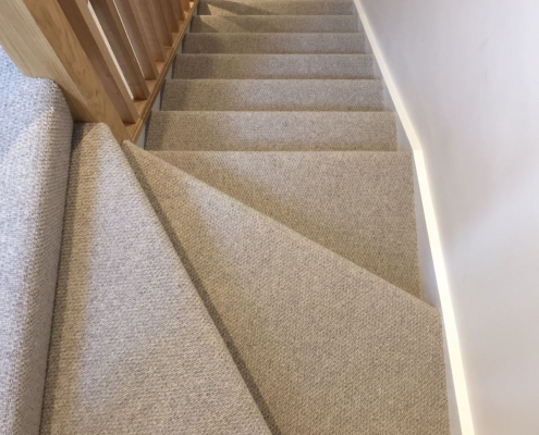 Wool loop Berber carpet fitted on kite winder staircase with white walls and oak bannister
