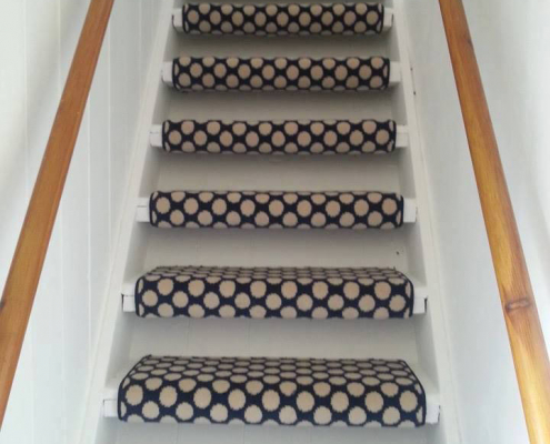 Black spotted wool carpet fitted to stair treads only on white painted staircase with wooden handrail