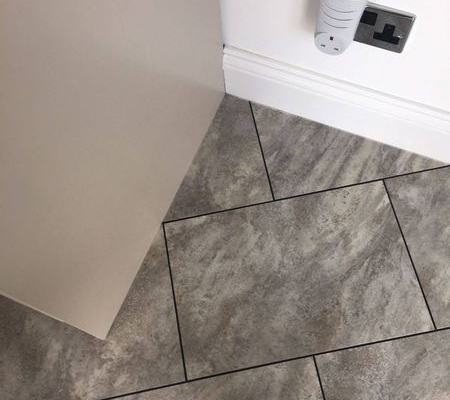 Close corner detail of pale grey slate rectangular LVT flooring with diagonal layout and design strips in kitchen