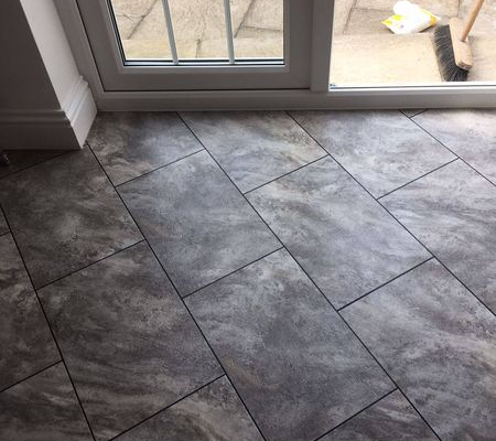 Pale grey slate effect rectangular LVT flooring laid diagonally with design strips in kitchen by patio doors