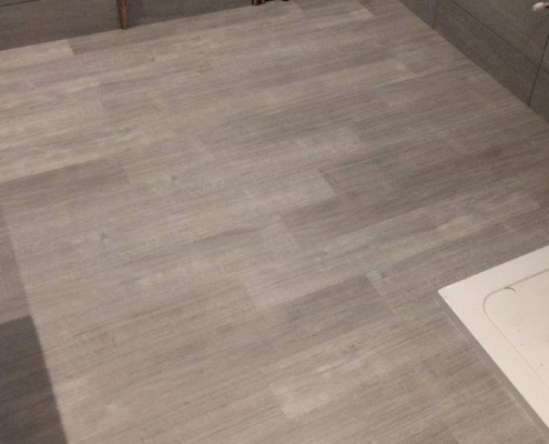 Grey oak plank LVT flooring in shower room with grey tiled walls viewed from opposite direction focusing on floor finish