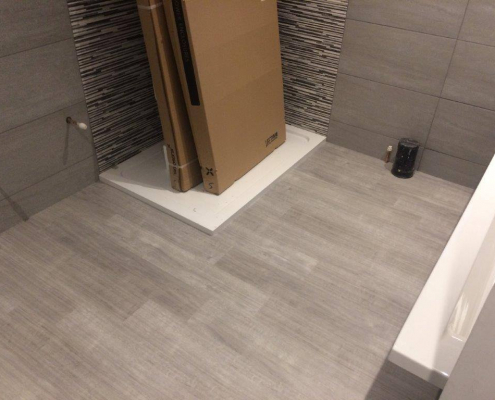 Shower room with grey tiled walls and grey oak plank LVT flooring facing walk-in shower with black and grey feature tiles