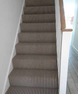 Staircase with black and cream striped wool loop carpet viewed from ground floor showing oak handrail and white banister detail