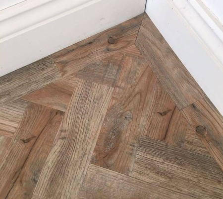Close corner detail of antique style herringbone parquet LVT flooring with decorative border in bright room