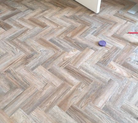 Antique style herringbone parquet LVT flooring mid installation in bright room with main body fitted and edges unfinished