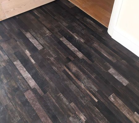 Close up of reclaimed dark strip wood LVT flooring installed by internal doorway in bright room