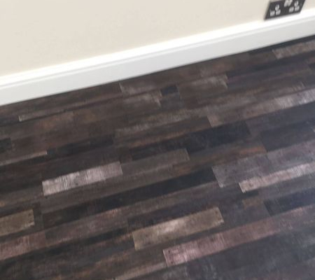 Close detail of reclaimed dark strip wood LVT flooring meeting skirting board in bright modern room
