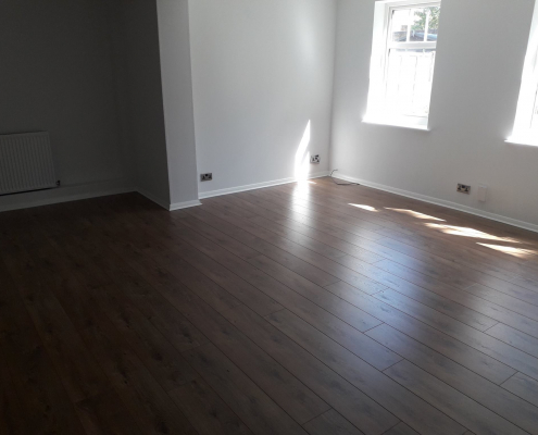 Oak effect laminate flooring in Redhill living room with white walls and view towards front window