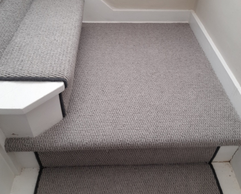 Grey loop berber stair runner with black whipped edges on staircase featuring large square turning step leading to landing in Redhill home
