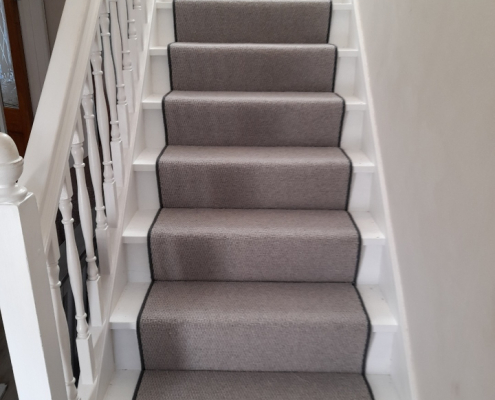Grey berber stair runner with black whipped edging installed on staircase in Surrey viewed from ground floor