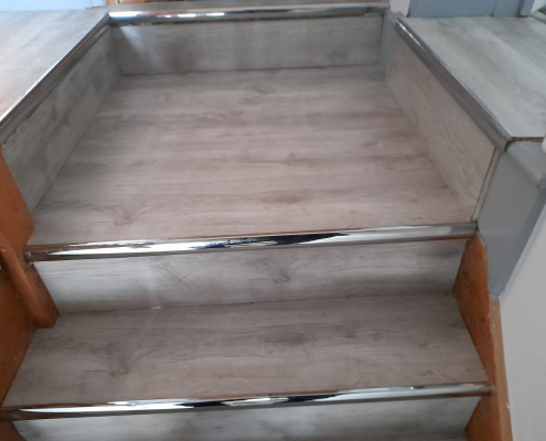 Large square top step with warm grey whitewashed LVT and chrome nosing in Surrey staircase leading to split landing