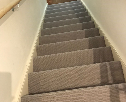View from top of stairs looking down on light soft grey wool loop berber carpet, showcasing the clean, soft texture and seamless transition to wooden flooring in Reigate home