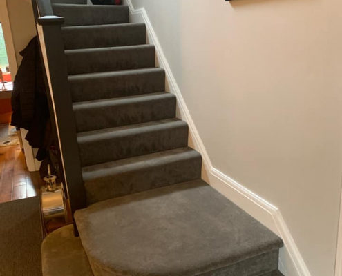 Charcoal velvet carpet staircase in Surrey with two large curved bottom steps leading from wooden flooring