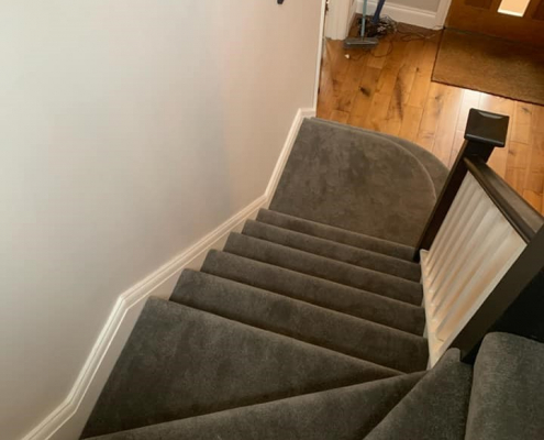 Charcoal velvet carpet stairs installation in Surrey viewed from top of staircase with white walls, black and white handrail, and wooden flooring below