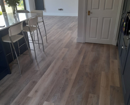 Long view through Surrey kitchen with limed washed oak LVT flooring leading to dining area and bifold doors