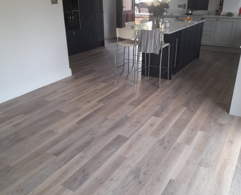 Limed washed oak LVT flooring in Surrey kitchen diner viewed from bifold doors with open dining area and mixed charcoal and light grey units