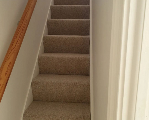Beige wool loop carpet fitted on enclosed staircase with walls both sides and oak handrail in Surrey home
