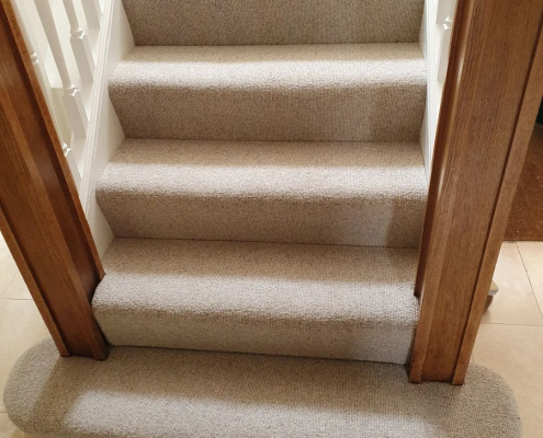 Detail of oat wool loop carpet on curved bottom stair next with oak newel post