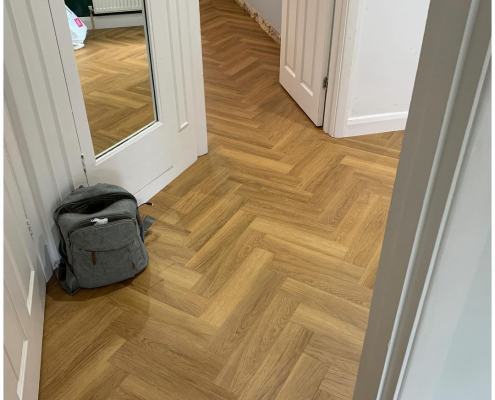 Honey oak herringbone LVT flooring in Surrey hallway with mirrored door and view into adjoining room