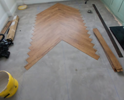 Wide view of Amtico warm oak herringbone LVT flooring installation in progress across a living room in Redhill Surrey showing layout planning and spacing