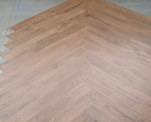 Close-up of installing Amtico warm oak LVT in a precise herringbone pattern, focusing on centre layout alignment in a Redhill Surrey living room