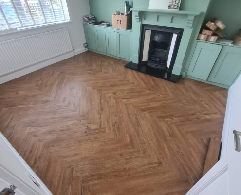 Finished Amtico warm oak herringbone LVT flooring in a bright living room with white walls, soft green feature wall, built-in cabinetry and black cast iron fireplace in Redhill Surrey