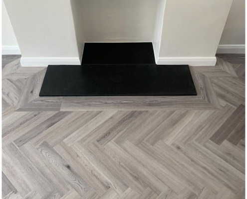 Close-up of light grey herringbone LVT flooring with border around contemporary fireplace in Redhill Surrey
