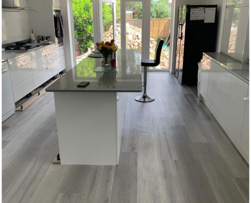 Full view of contemporary white kitchen with grey ash plank LVT flooring and garden through French doors