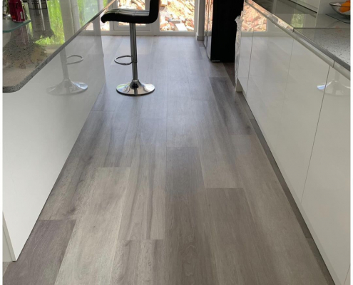Grey ash plank LVT flooring in contemporary white kitchen with island and French doors leading to garden