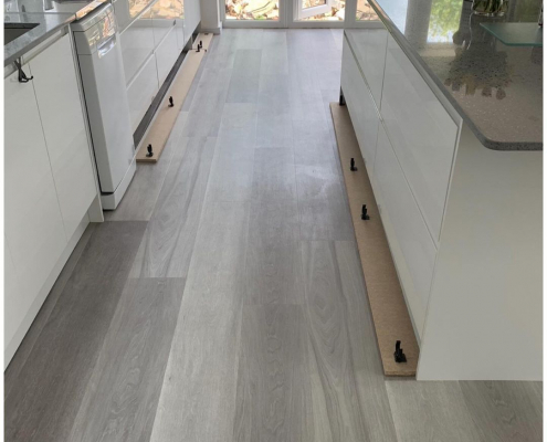Grey ash plank LVT flooring in contemporary white kitchen with island and French doors leading to garden