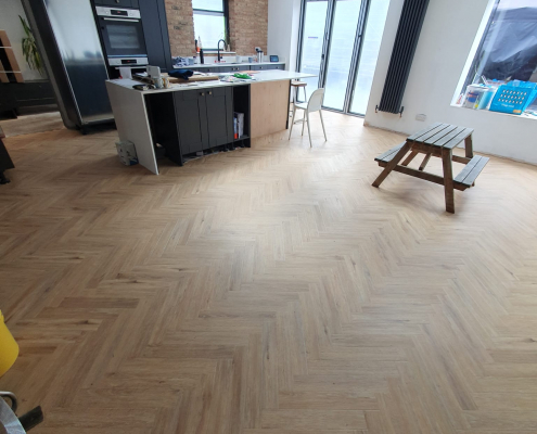 Wide view of open plan ground floor in Surrey with Project Floors warm oak herringbone LVT flooring leading towards kitchen and bifold doors