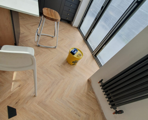 Close-up of Project Floors warm oak herringbone LVT flooring next to bifold doors showing detailed pattern and natural light in Surrey home