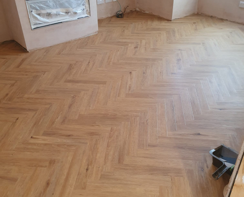 Project Floors warm golden oak herringbone LVT flooring in a finished Surrey lounge with a bright bay window and natural light