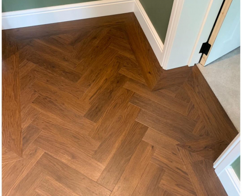 Close-up of Amtico Black Walnut herringbone LVT flooring showing warm natural wood tones and pattern detail