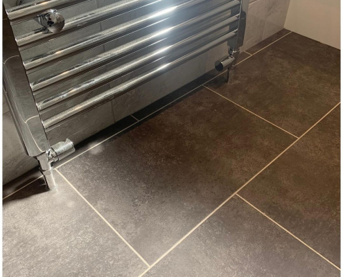 Close-up of graphite stone effect LVT flooring next to chrome towel radiator showing texture and brick pattern detail