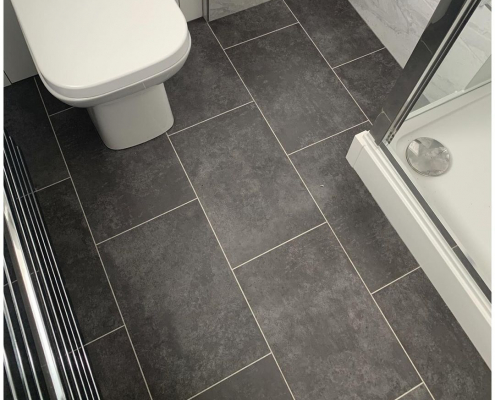 Graphite stone effect LVT flooring in Redhill bathroom with white suite, glass shower screen and marble wall tiles