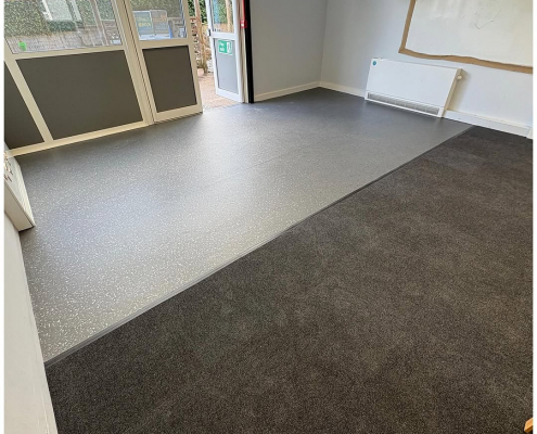 School classroom with grey and white safety flooring next to dark grey carpet