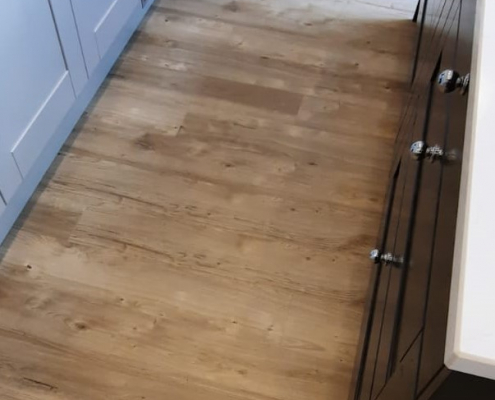 Sun bleached oak LVT kitchen flooring Close up of light sun bleached oak LVT flooring installed between grey kitchen cupboards and navy blue island in Reigate kitchen