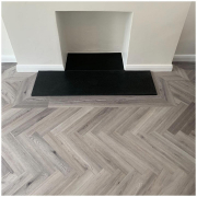 Close-up of light grey herringbone LVT flooring with border around contemporary fireplace in Redhill Surrey