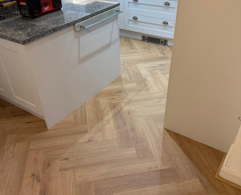 Warm Oak Herringbone Laminate Flooring Detail Close-up of Furlong Manor warm oak herringbone laminate flooring between kitchen and dining areas with natural wood tones and detailed parquet effect finish.