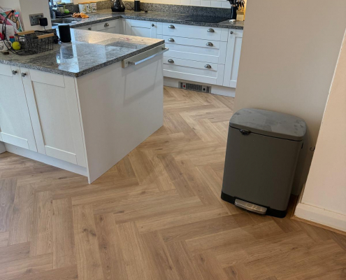 Furlong Manor Herringbone Laminate in Open Plan Kitchen Diner Furlong Manor warm oak effect herringbone laminate flooring installed in an open plan kitchen diner with grey shaker kitchen units, granite worktops and glazed French doors in Redhill Surrey.