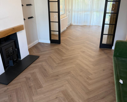 Finished Herringbone Flooring Across Open Plan Living Space Finished Furlong Manor warm oak herringbone laminate flooring extending from living room through to dining area in modern Surrey home.
